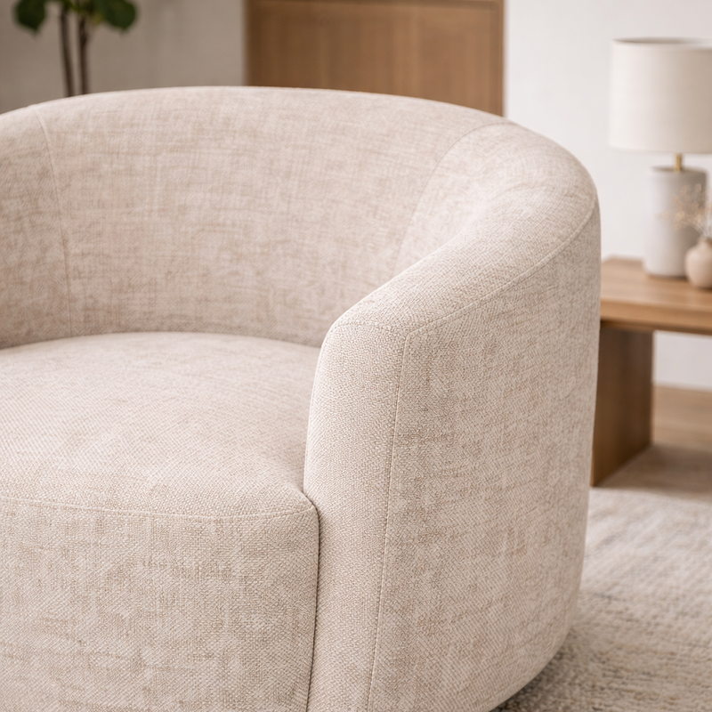 Beige armchair in a living room setting with a lamp and plant in the background.
